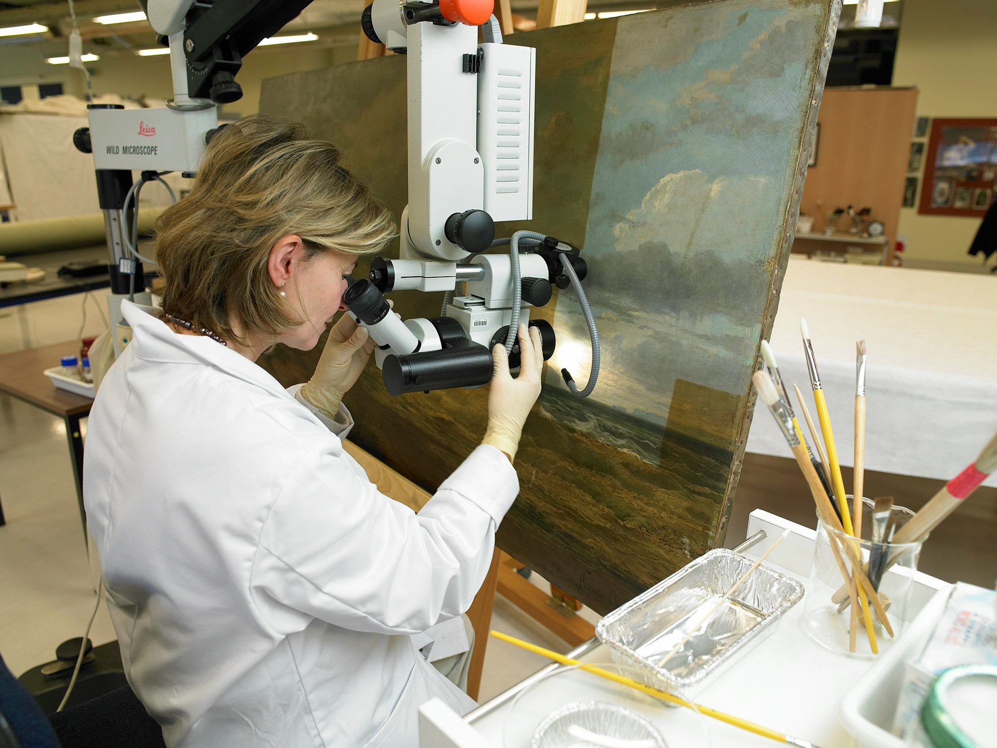 A woman looking at a painting through a piece of scientific equipment