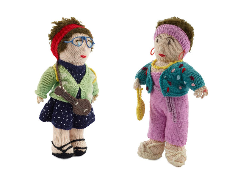 Two knitted dolls. Left: A woman with a red headband, wearing glasses, in a blue dress with white polkadots and a green cardigan. On the right: A woman in pink headband and dungarees with turquoise cardigan and yellow handbag