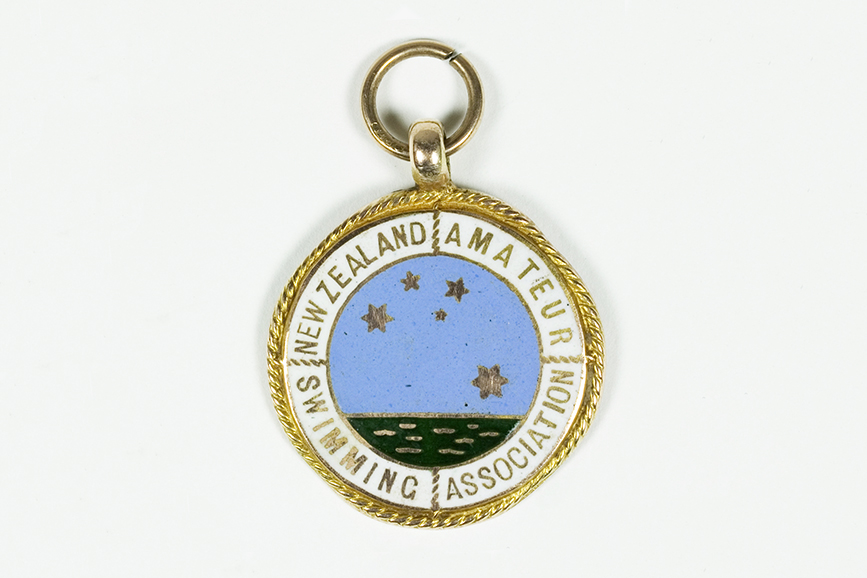 A round badge with gold edging and an image of the sea with the Southern Cross in stars above it. It has the words New Zealand Amateur Swimming Association on it