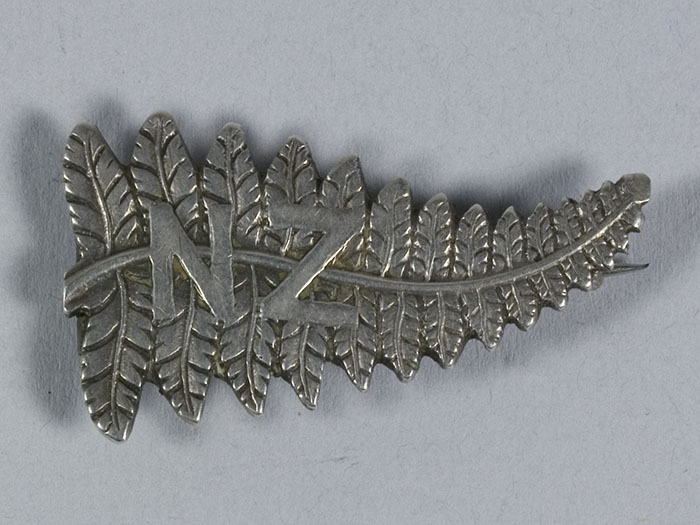 Brooch in the shape of a silver fern with the letters N and Z on it