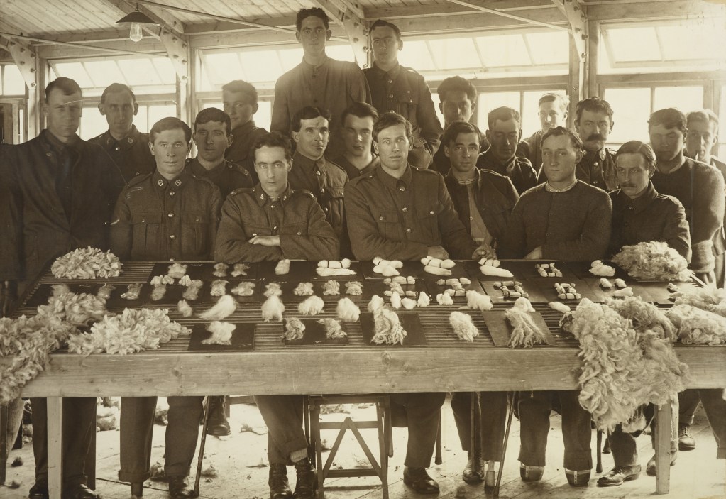 Twenty soldiers sit at a table with wool displayed on it
