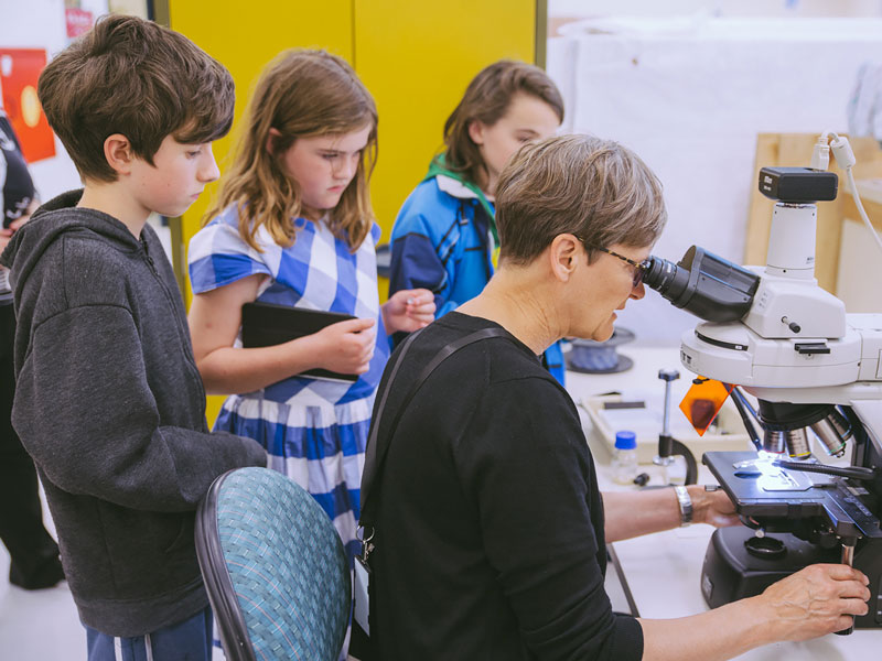 Young school children watch a painiting conservator at work