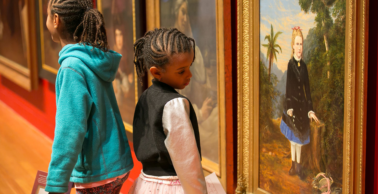 Two girls look closely at the portrait wall