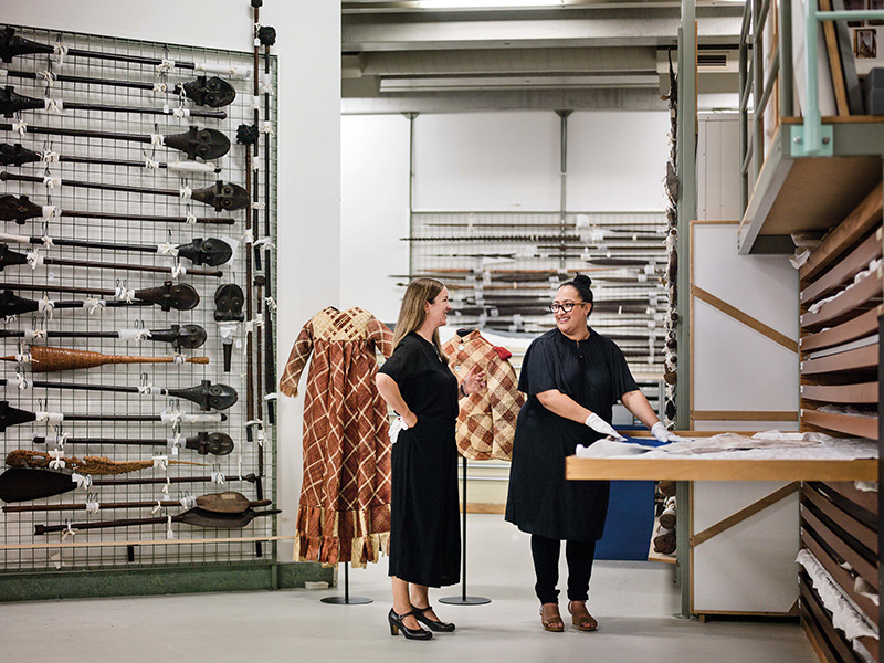 Two women stand in a museum store room looking at objects in a drawer