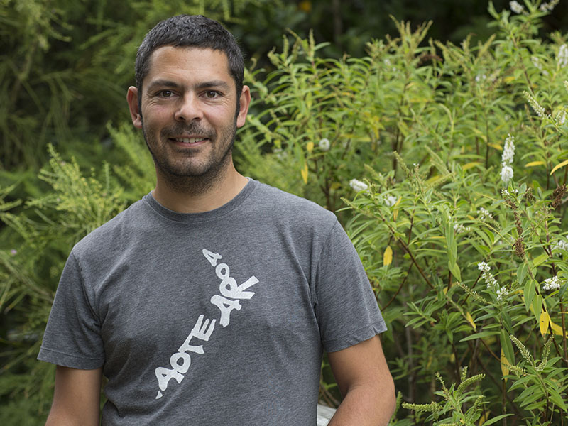 Carlos poses outdoors in front of a large plant