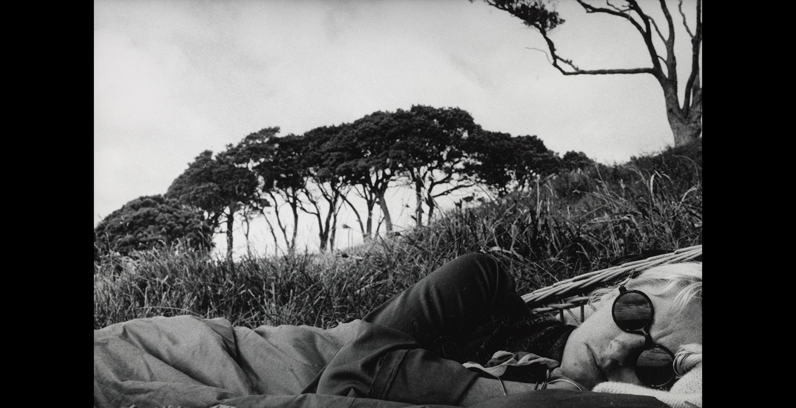 Woman lies on the ground looking into the camera with grass and trees behind her