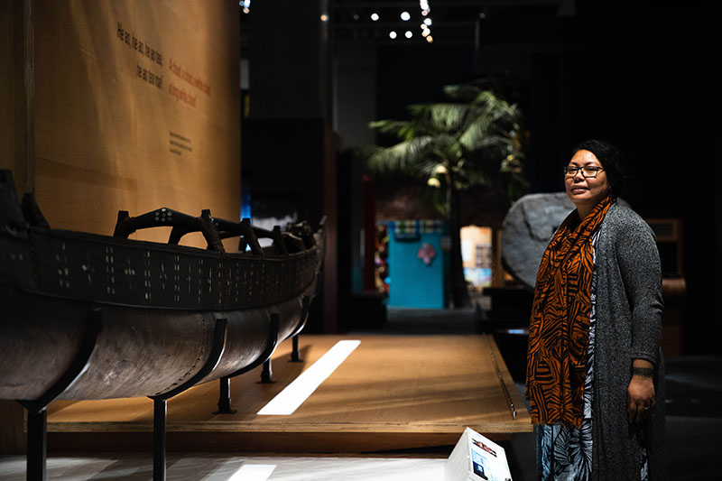 Safua stands to the right of the photo frame in front of a waka