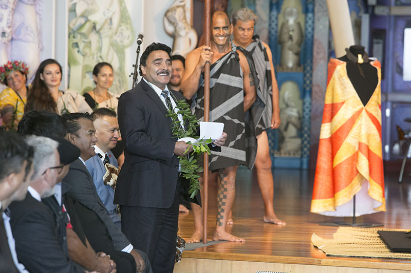 Arapata addresses the room standing in front of a cloak draped on a mannequin