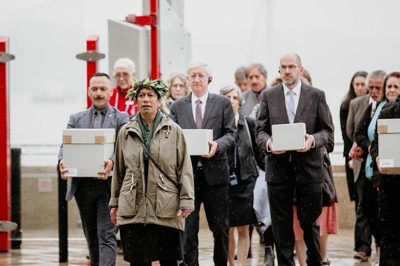 A group of people enter a building. Three of them carry boxes