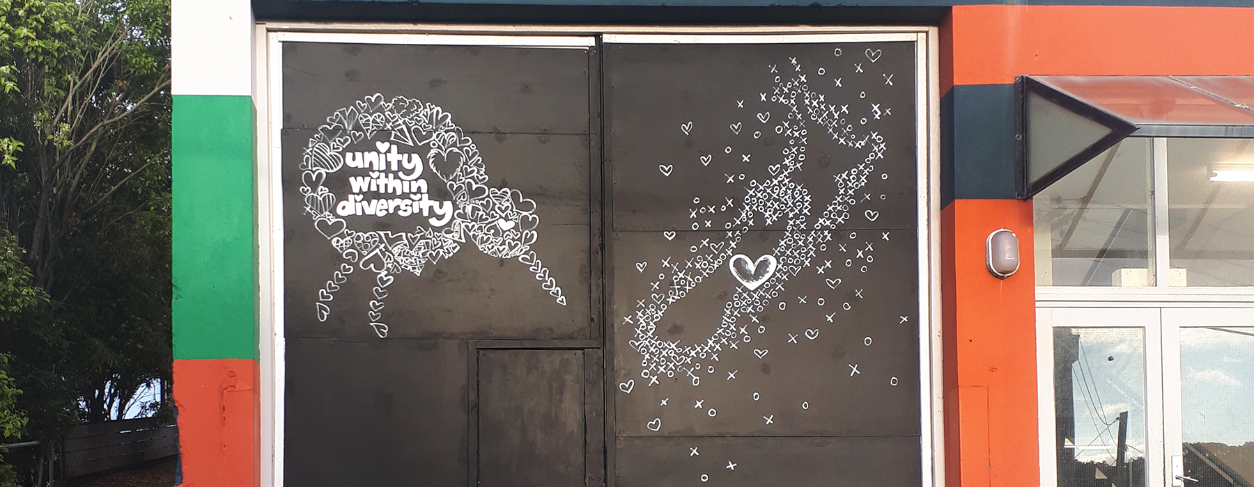 A black sign on a garage that has a white kiwi and a map of New Zealand drawn on it with the words "Unity within diversity"