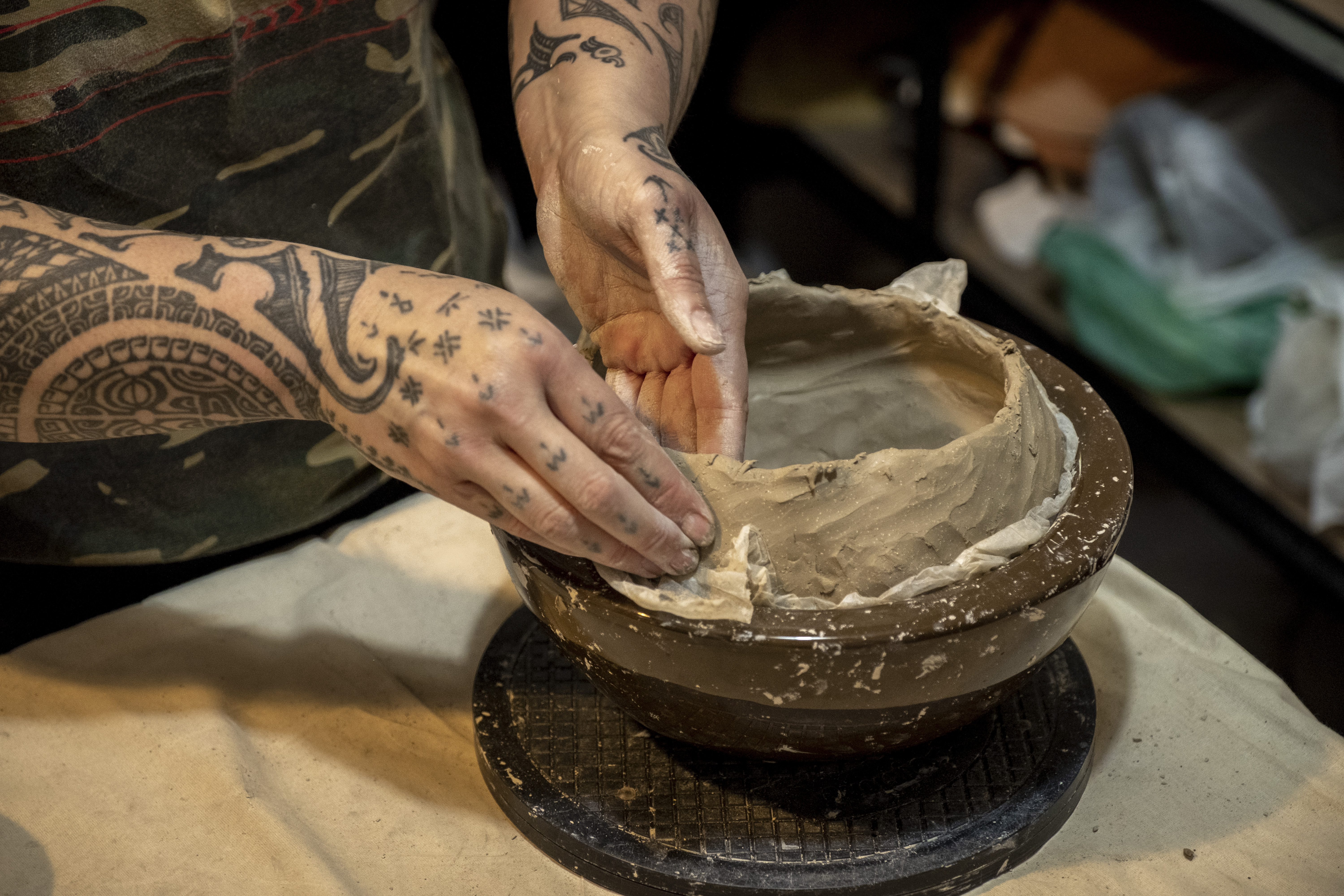 Two hands working on a piece of unfired clay pottery.