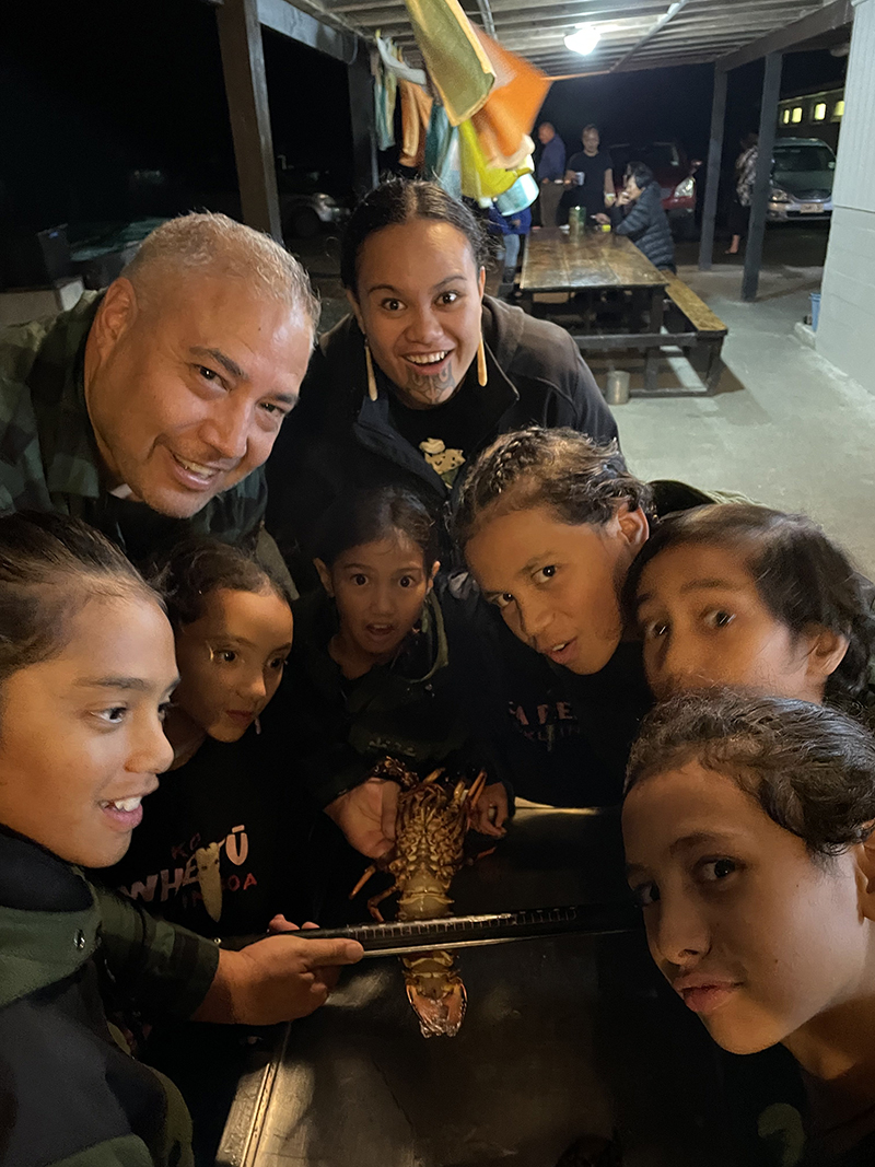 A man and woman and several children are huddled together and looking at the camera. The man is holding a crayfish and a ruler.