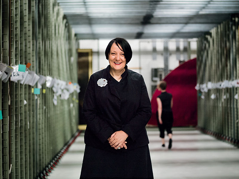 Charlotte poses in front of the racks that house paintings. A woman walks past behind her