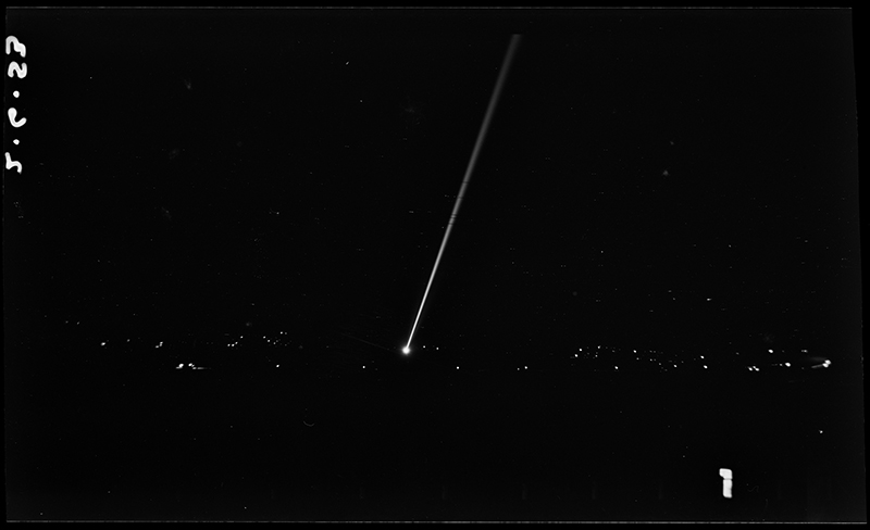 A largely black photo with a single long white beam of light and some other white dots indicating lights