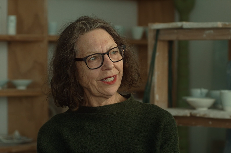 A woman talking to someone off screen and sitting in an artist studio.