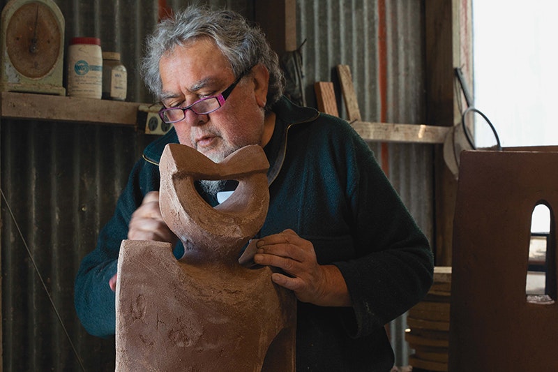 A man in a workshop working with a clay sculpture