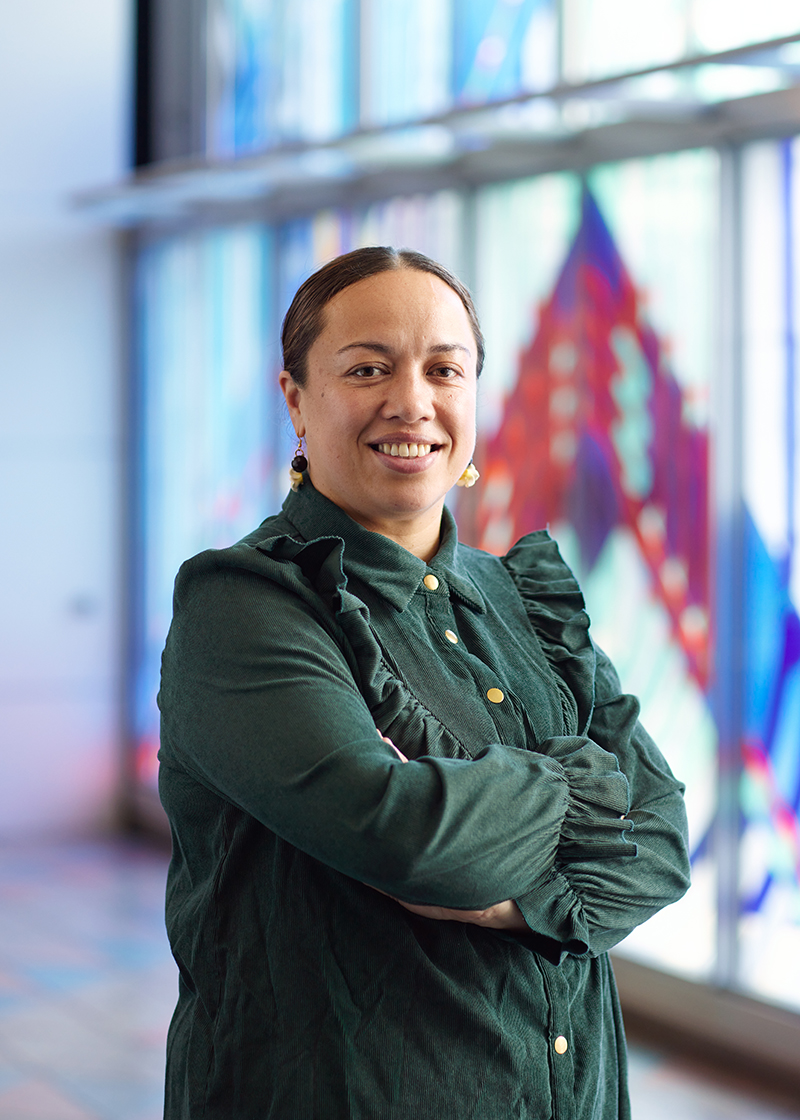 A woman in a green top and her hair pulled back is standing at an angle and smiling at the camera.