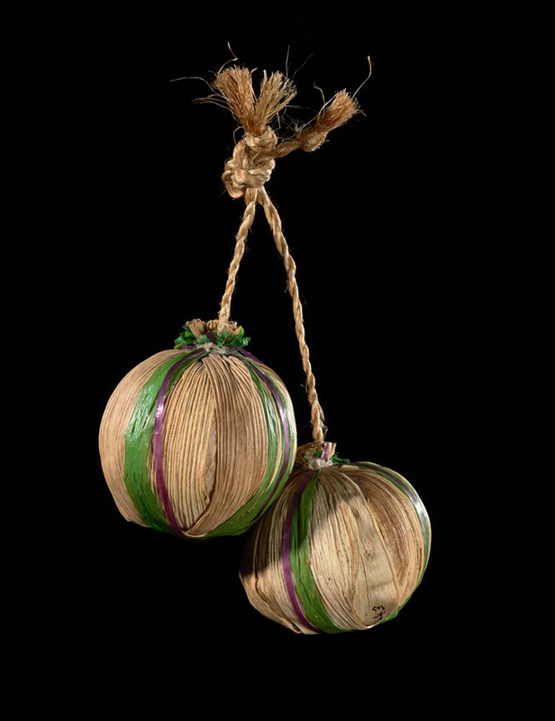Two balls made from flax and rafia with a cord each are hanging on a black background.