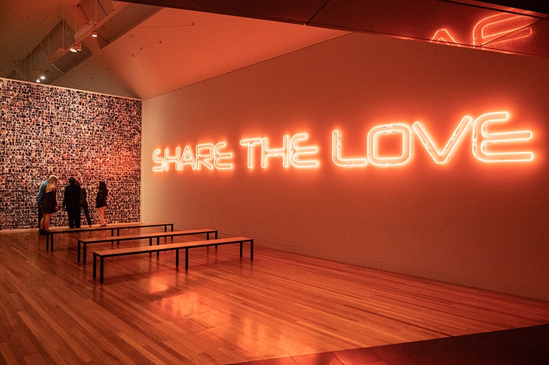 People in a large room that has a giant neon sign that says Share the love.
